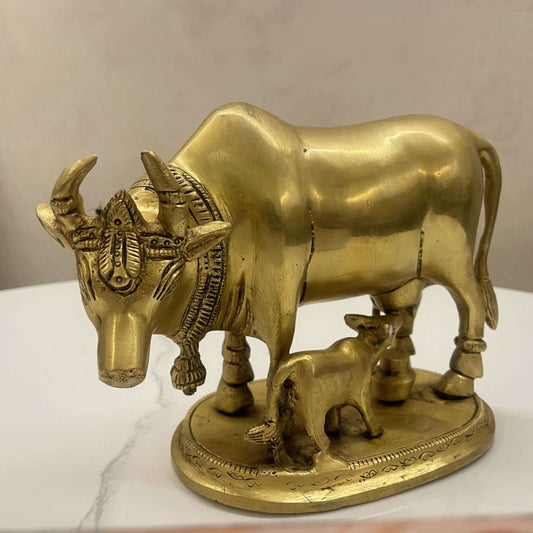 Front-angle view of the brass Kamadhenu cow and calf idol highlighting the intricate carvings on the head and decorative bell.