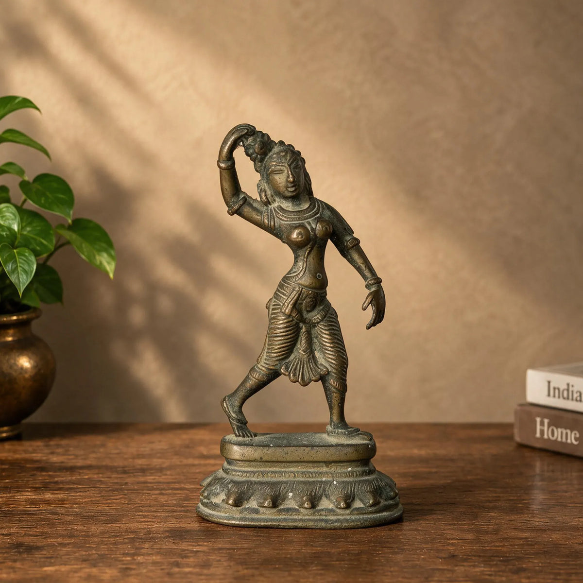 Antique brass dancing apsara statue on a wooden table beside a brass vase
