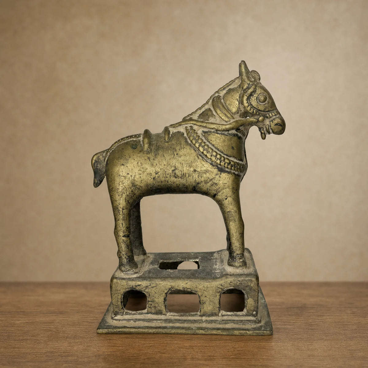 Antique brass horse statue on a pierced base, front view on a wooden table