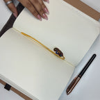 Brass floral bookmark with red enamel multicolor floral motif marking pages in an open notebook