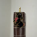 Brass rabbit bookmark with black enamel and pink accents on leather journal spine