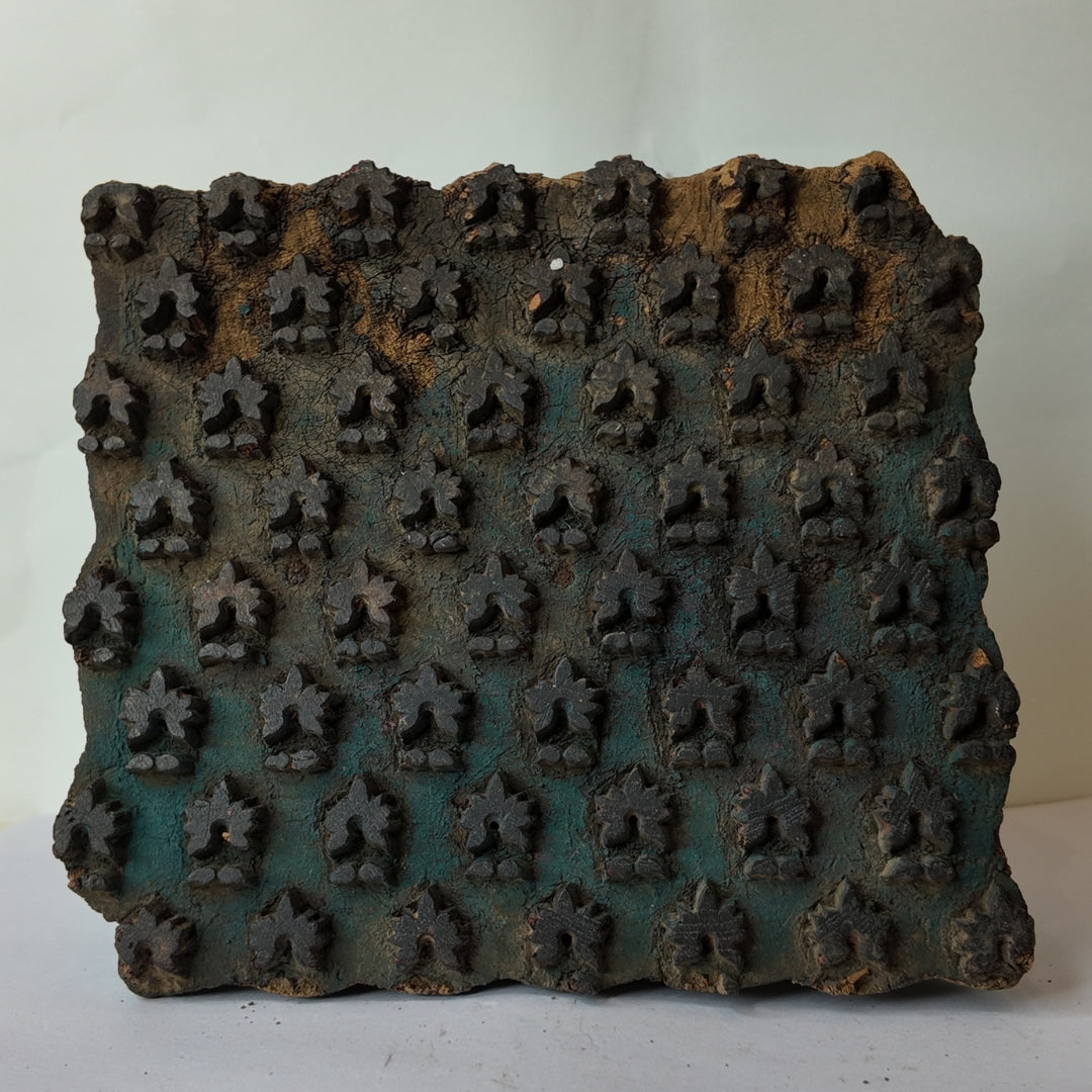 Front view of a square vintage Indian hand-carved wooden printing block showcasing rows of repeating three-pointed trefoil crown buds against a heavily distressed turquoise and teal green stained background patina