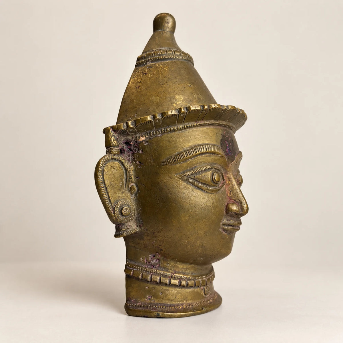 Side profile of the antique brass Gauri mask showing crown and earring detail
