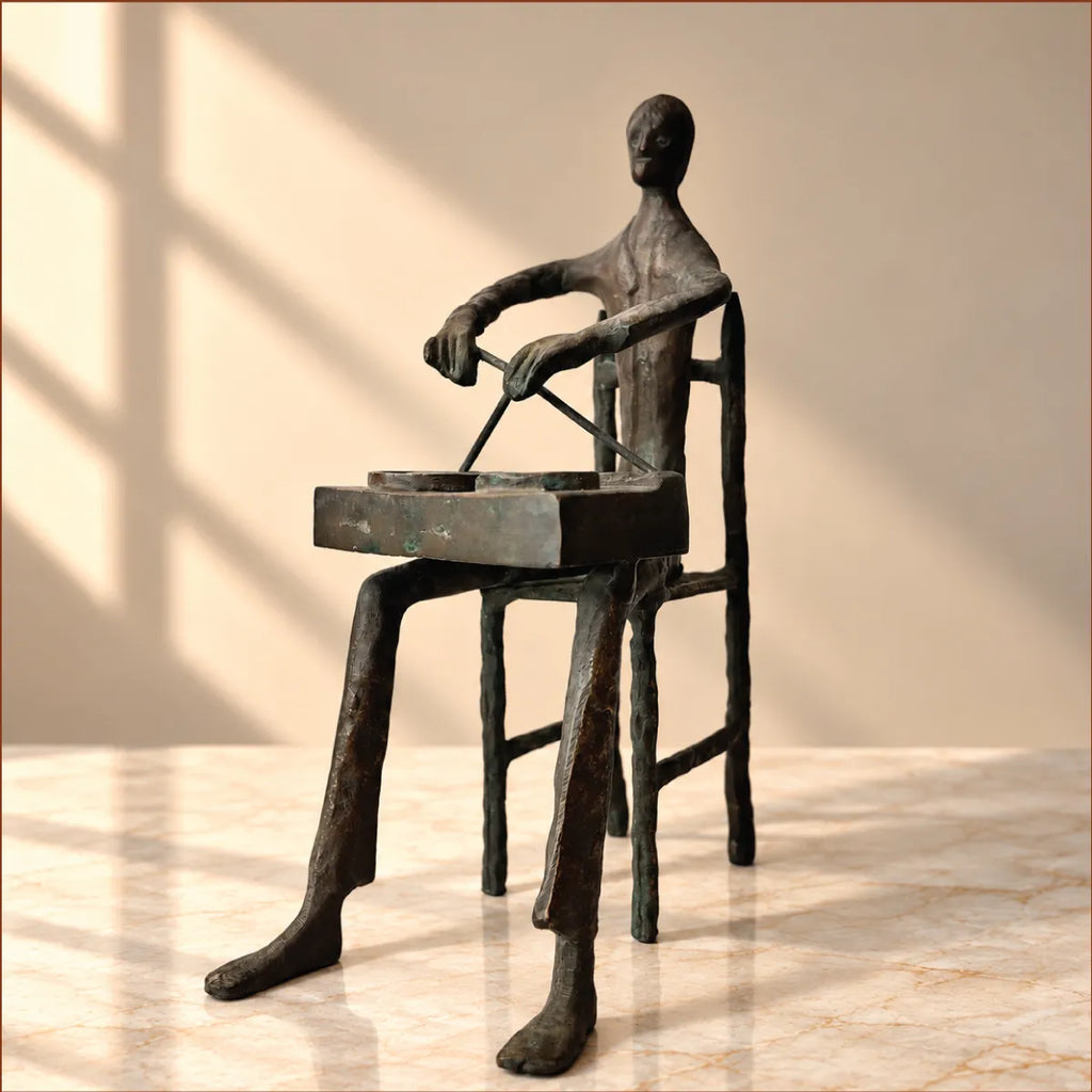 Side view of the antique brass tribal musician figurine seated on a chair with elongated legs
