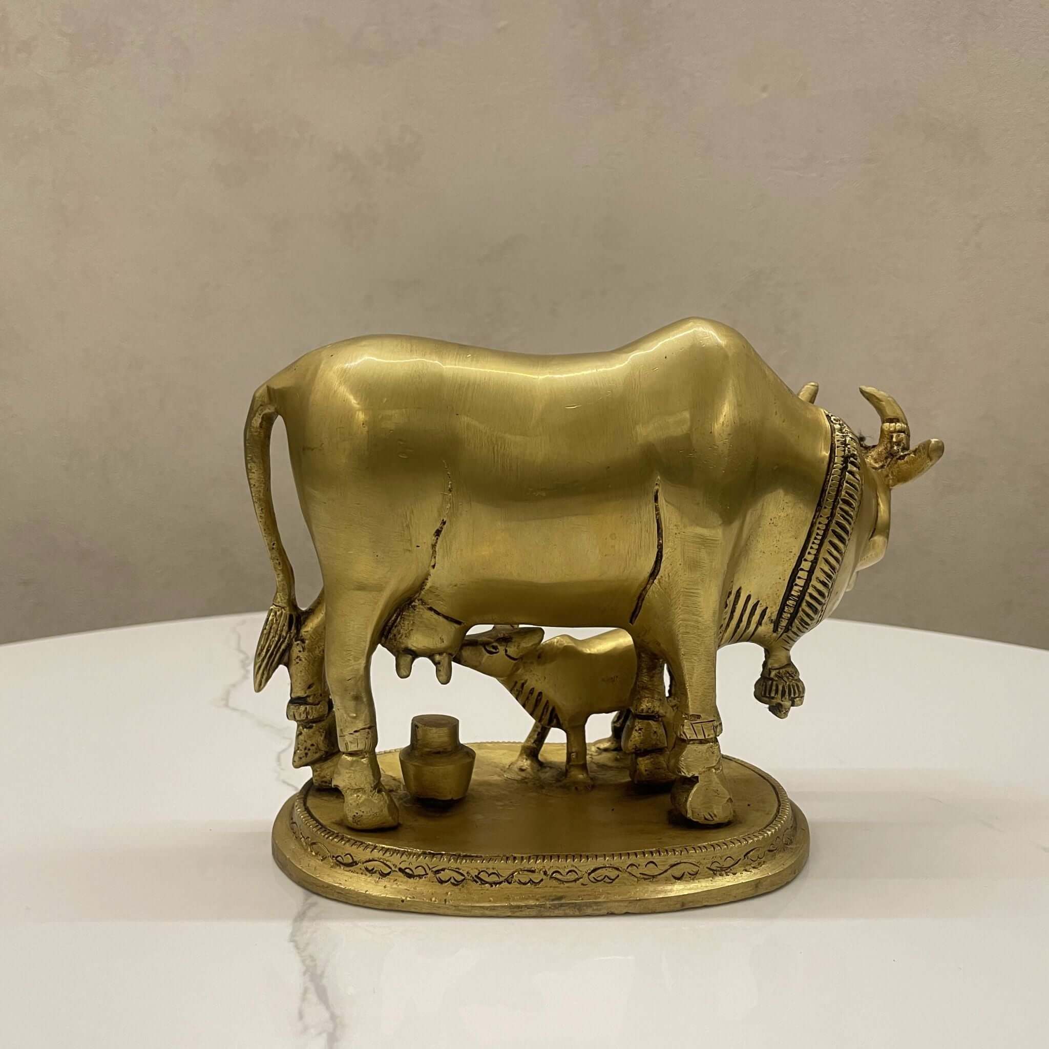 Side view of a solid brass cow and calf (Kamadhenu) statue showing detailed craftsmanship and a small pot.